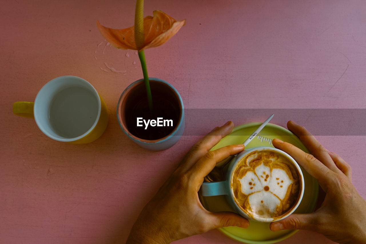 CLOSE-UP OF HAND HOLDING COFFEE CUP WITH SPOON