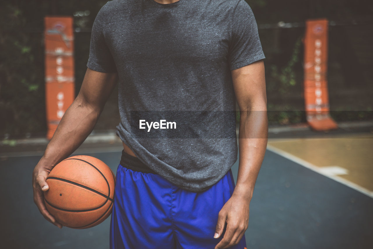 Midsection of man holding basketball ball on court