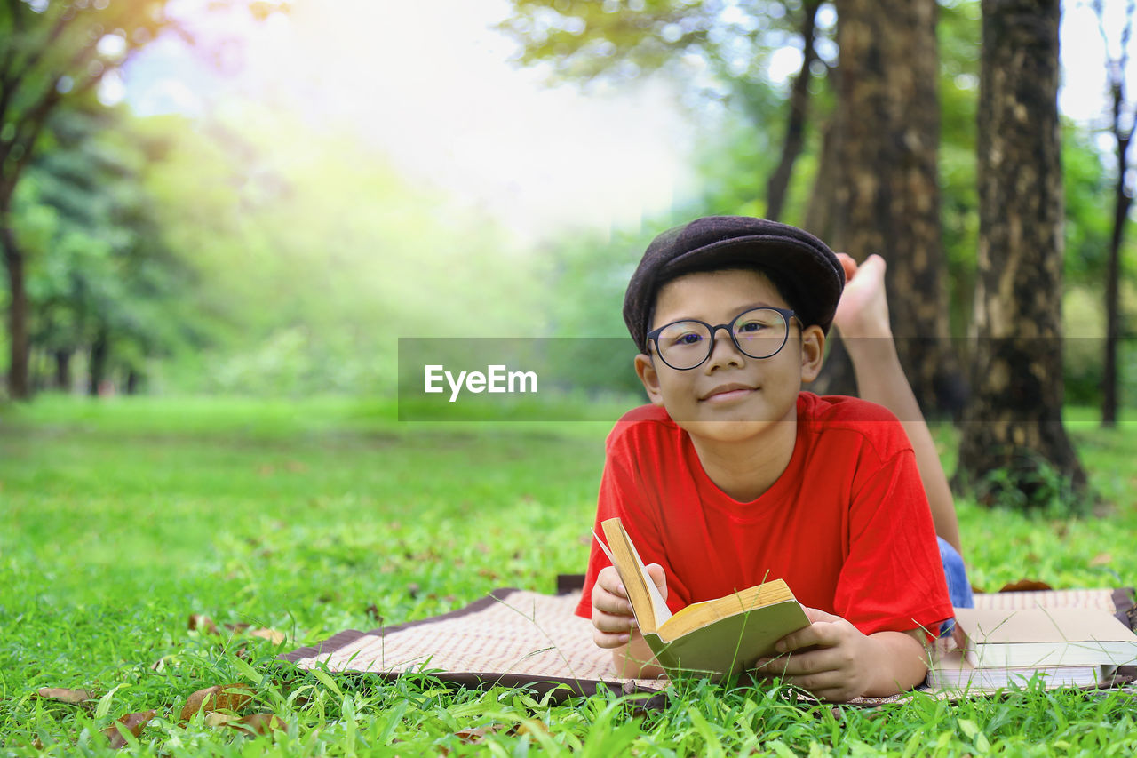 Portrait of boy holding book while lying on field