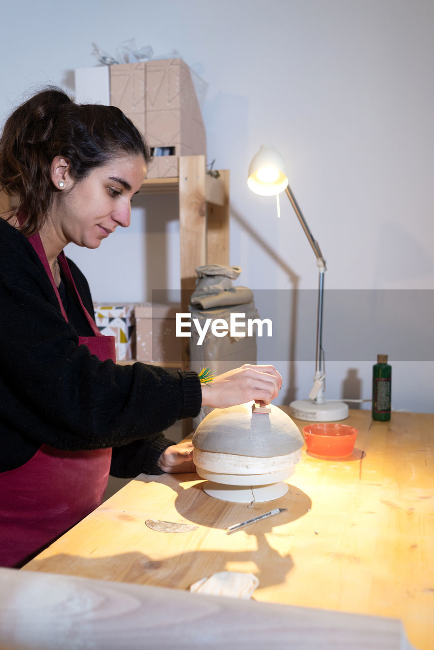 Young ceramist woman marking ceramic bowl in pottery workshop