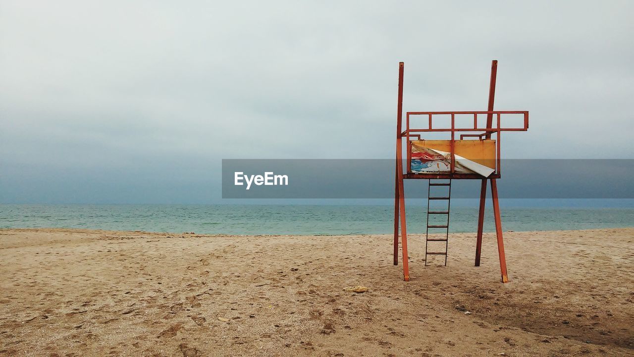 Empty lifeguard chair on beach against sky