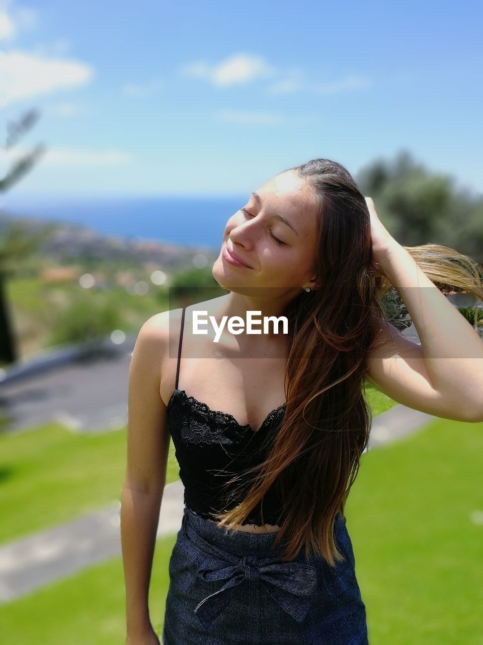 Beautiful young woman with hand in hair standing outdoors on sunny day