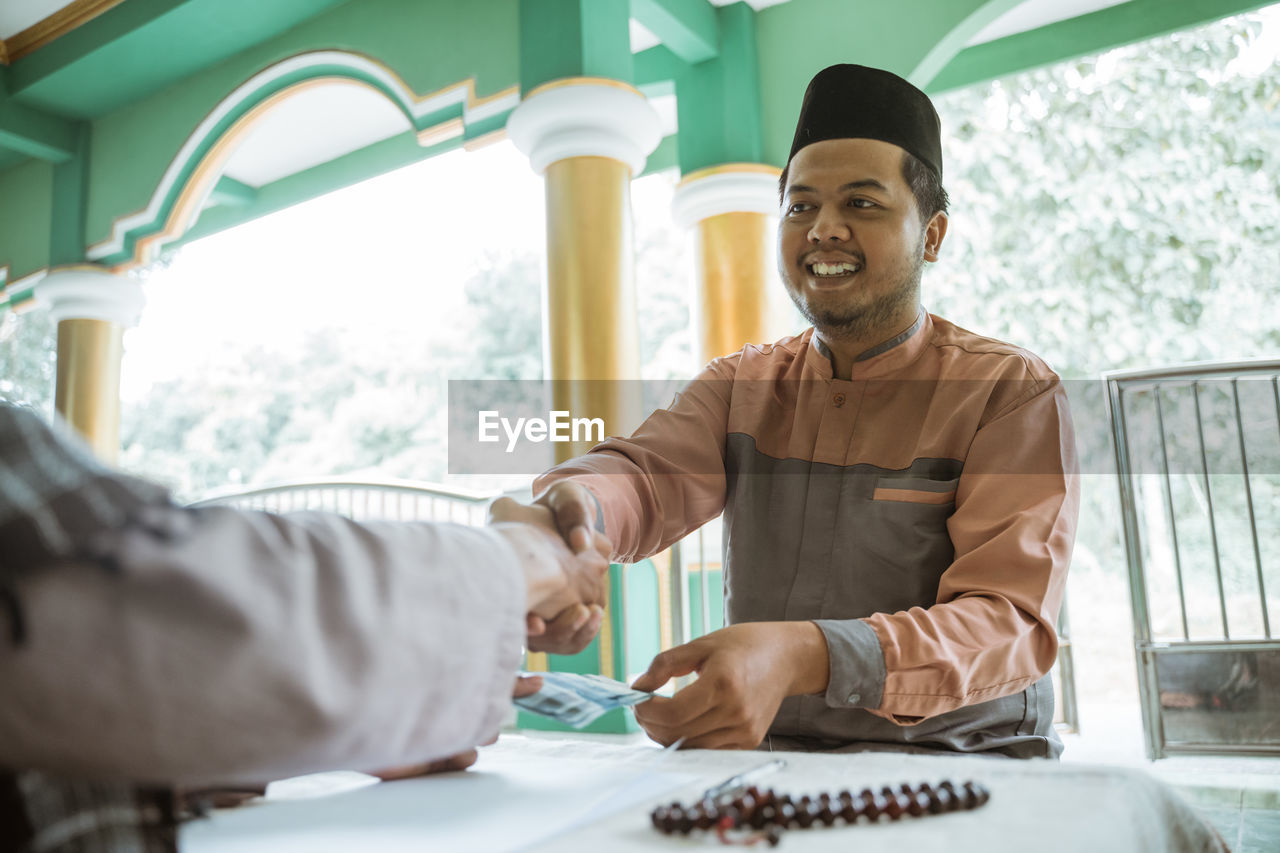 Happy young man shaking hand with friend at mosque