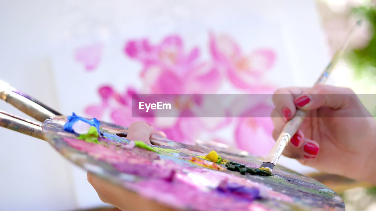 Female hands, painter, artist paints a picture of flowers, she holds palette with paints and brushes