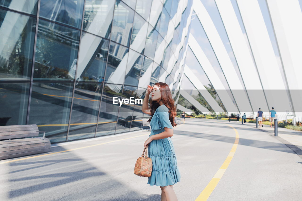 Side view of young woman standing on road in city