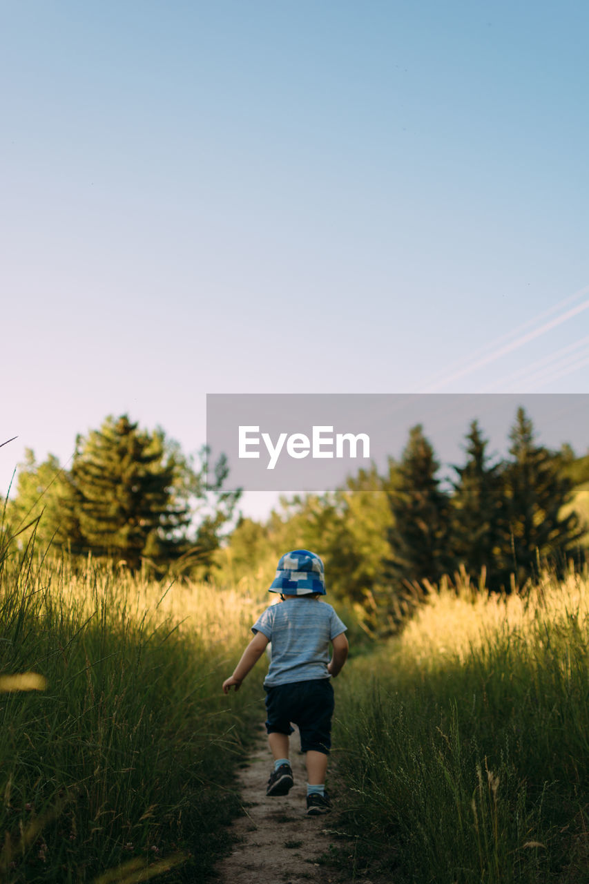 Rear view of boy walking on field against clear sky