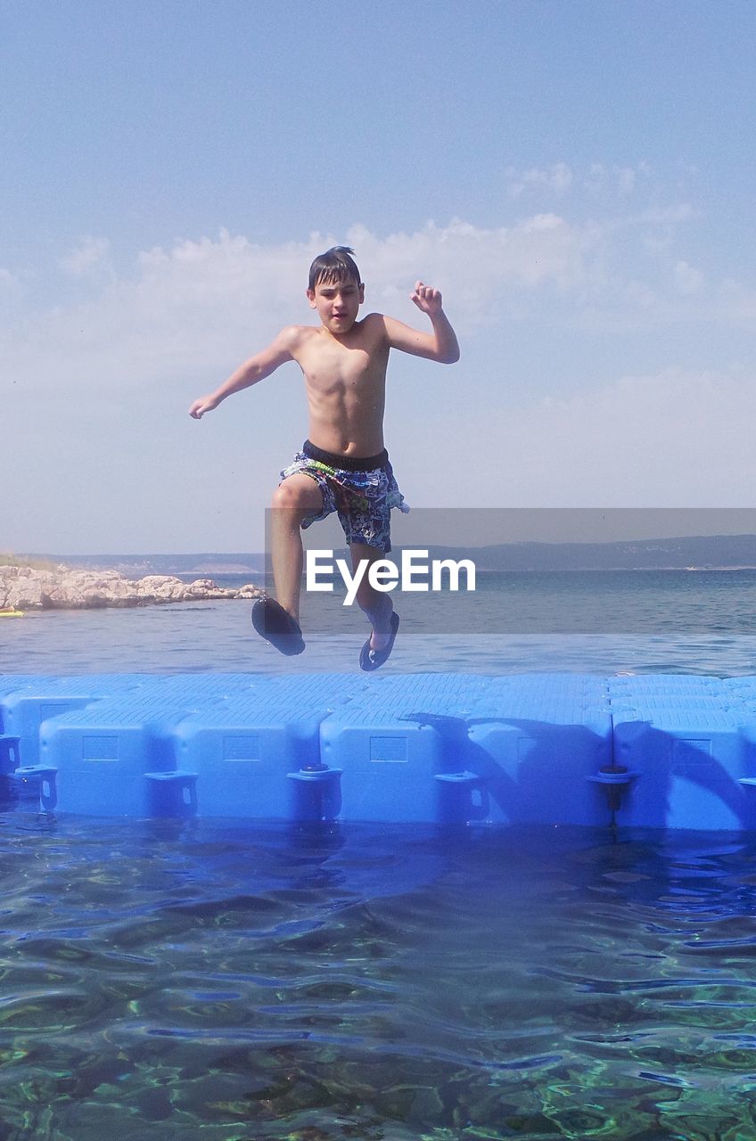 Shirtless boy jumping in sea against sky