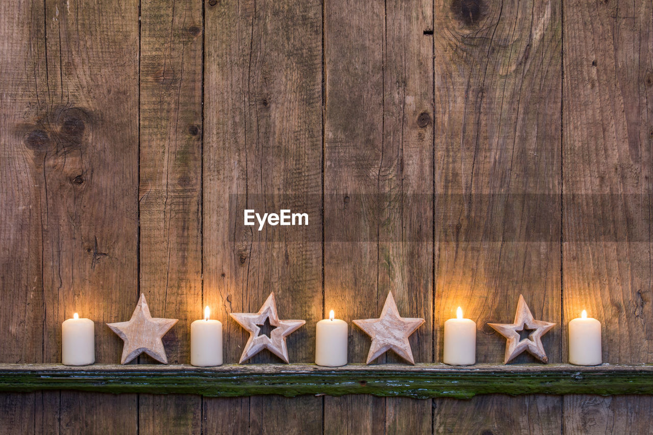 Illuminated candles with star shape decorations on wooden fence during christmas
