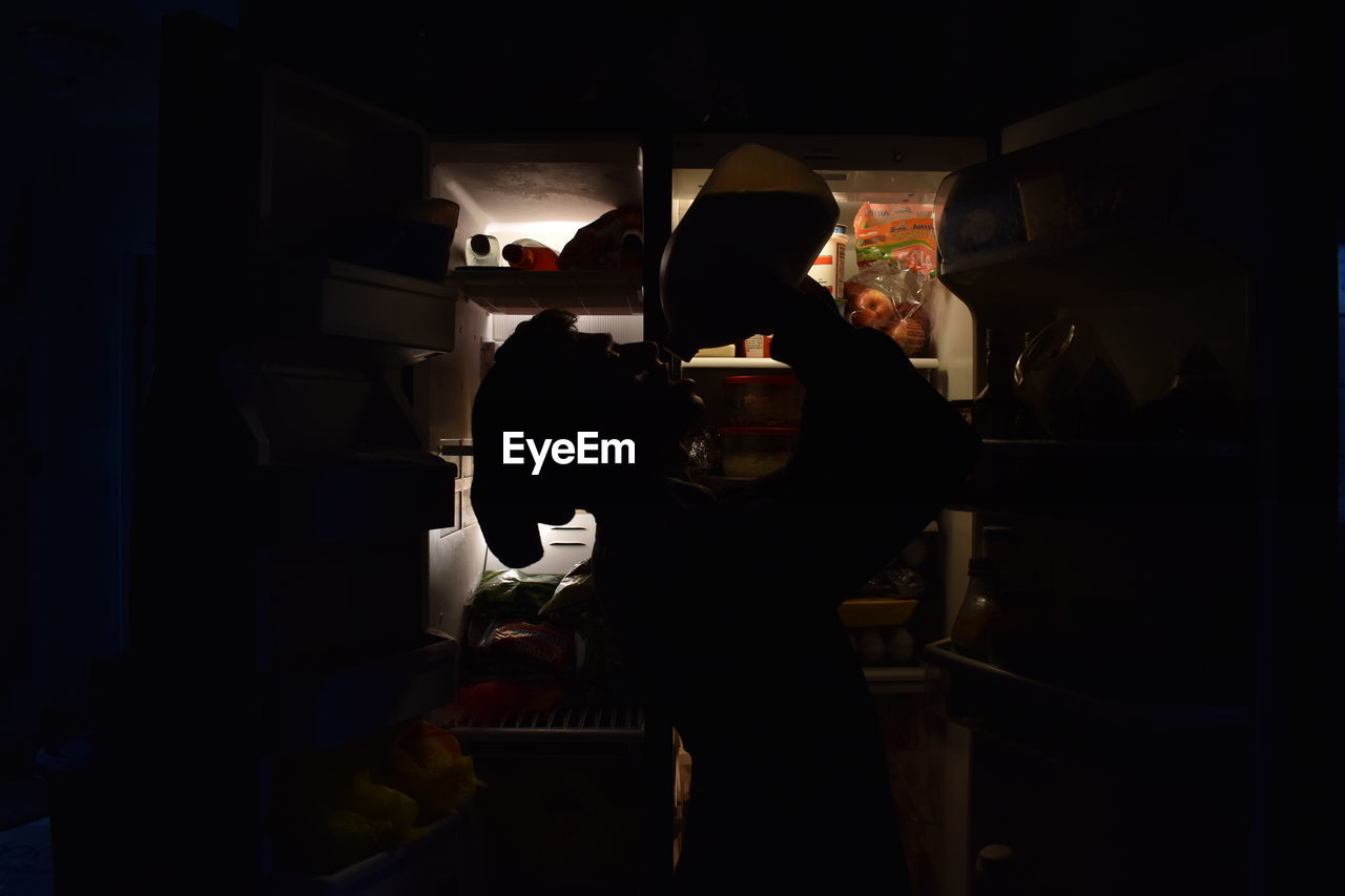 Side view of silhouette man drinking while standing by refrigerator at home