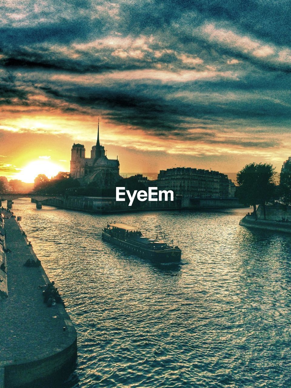 Boat in river with buildings against clouds at sunset