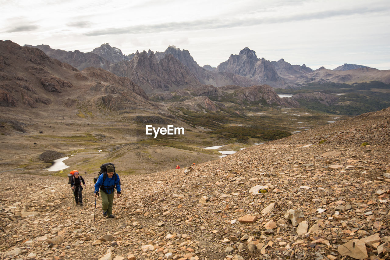 REAR VIEW OF PEOPLE WALKING ON MOUNTAIN ROAD