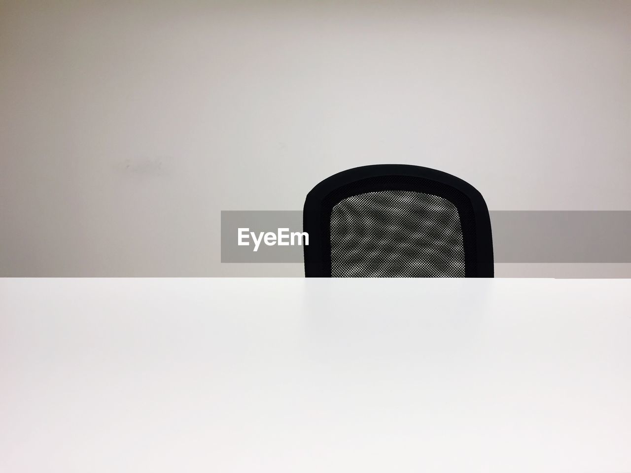 White office table in front of black chair against wall