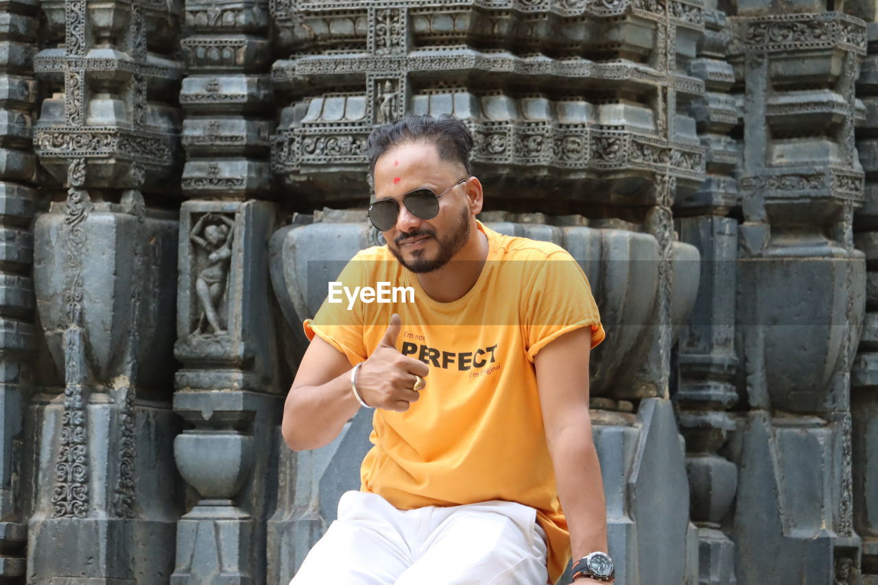 temple, one person, architecture, adult, men, glasses, sunglasses, front view, fashion, three quarter length, person, casual clothing, built structure, day, portrait, sitting, ancient, clothing, history, smiling, outdoors, travel, building, leisure activity, lifestyles, travel destinations, temple - building