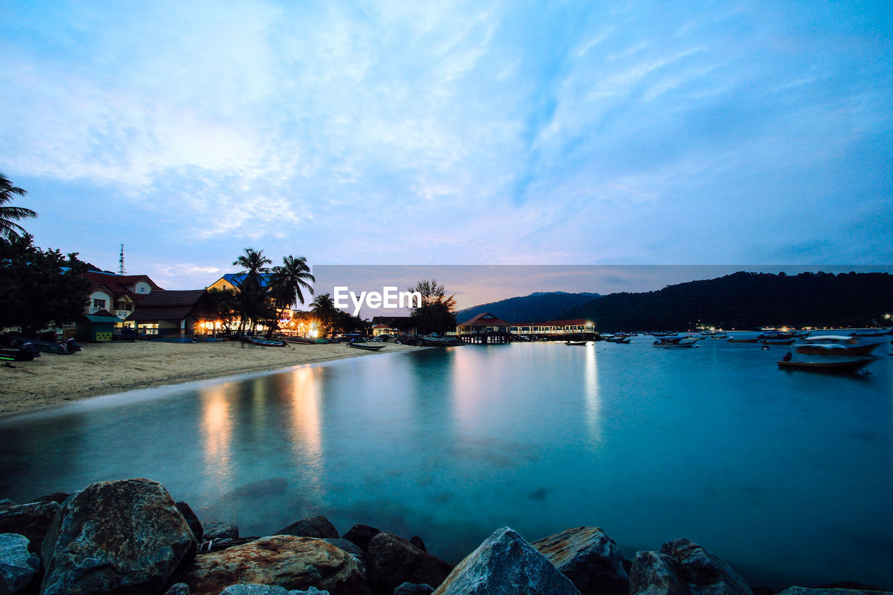 Sea by illuminated buildings against sky