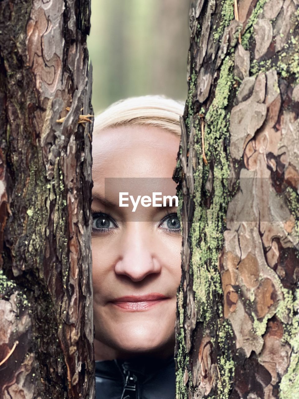 CLOSE-UP PORTRAIT OF SMILING WOMAN AGAINST TREES