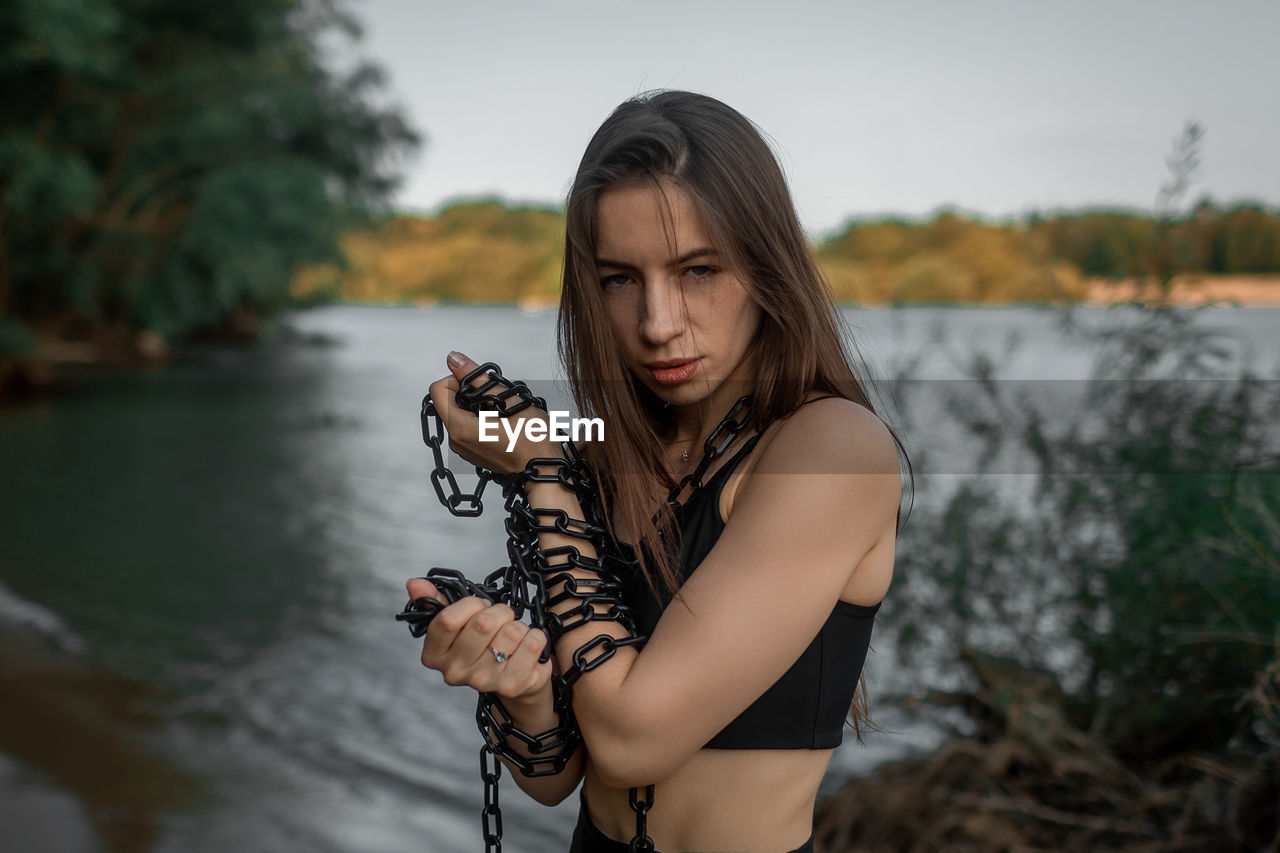 Portrait of young woman standing against lake during sunset