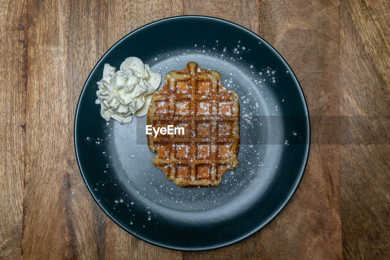 High angle view of waffle with whipped cream and powder sugar in plate on table