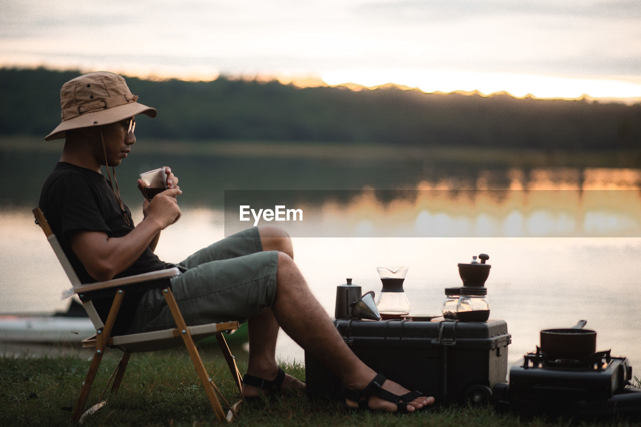 MAN SITTING ON CHAIR BY LAKE