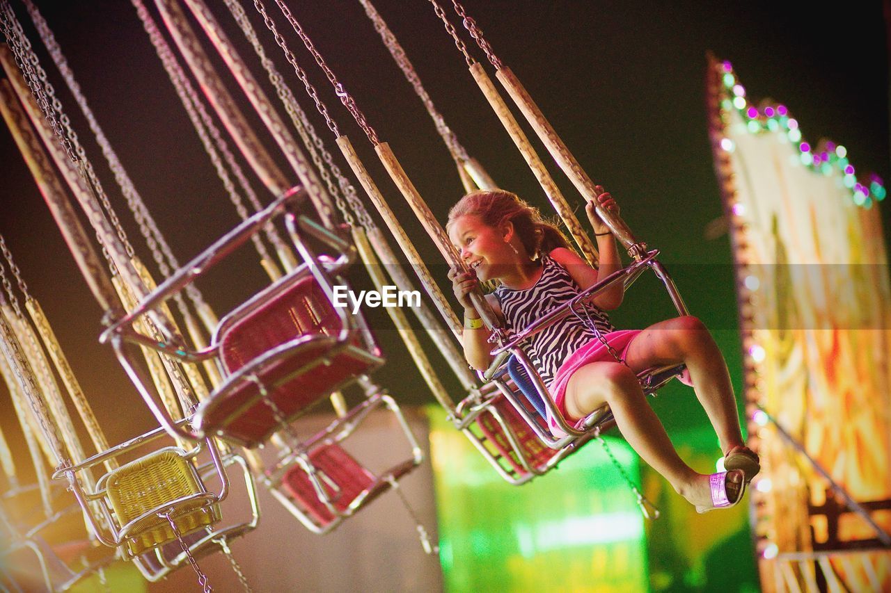 Smiling girl looking away while sitting on chain swing ride