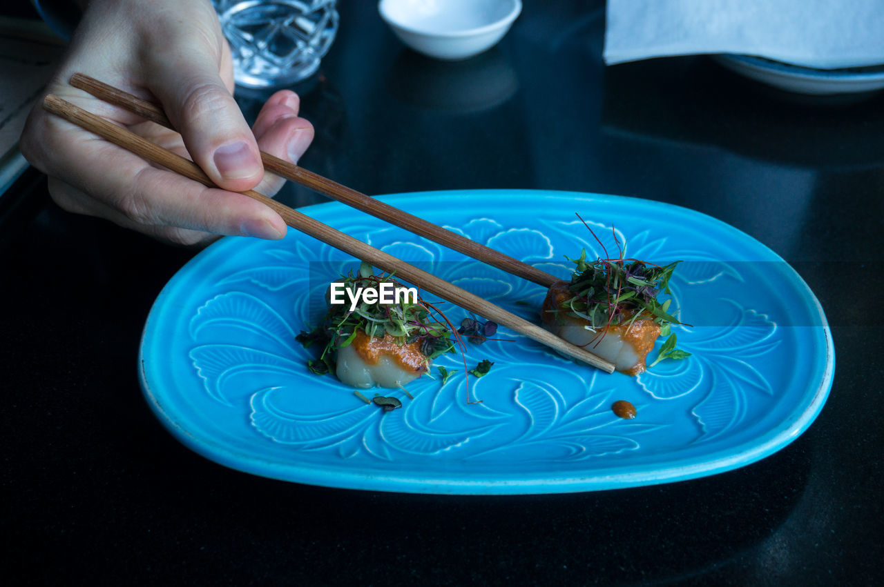 Eating raw scallop dish served with herbs and sauce with chopsticks. japanese restaurant background