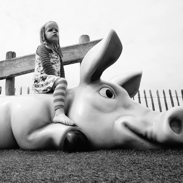 Low angle view of cute girl sitting on pig sculpture in park