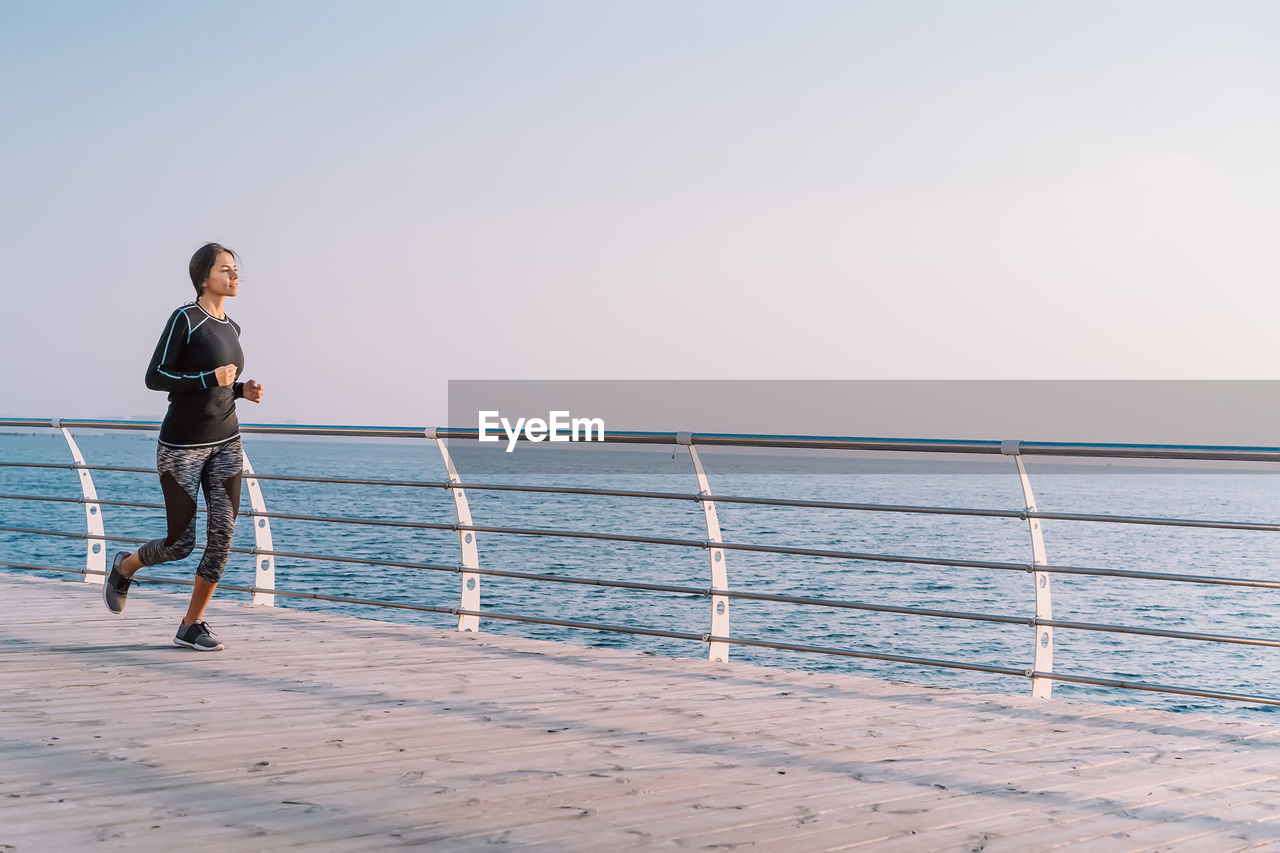 Full length of man standing on railing against sea