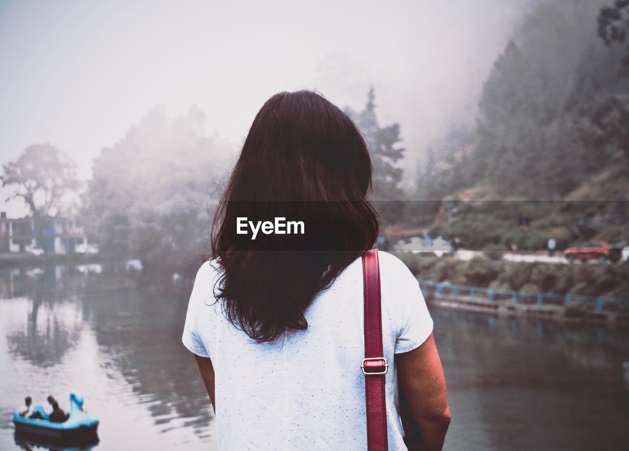 Rear view of woman standing by river against sky