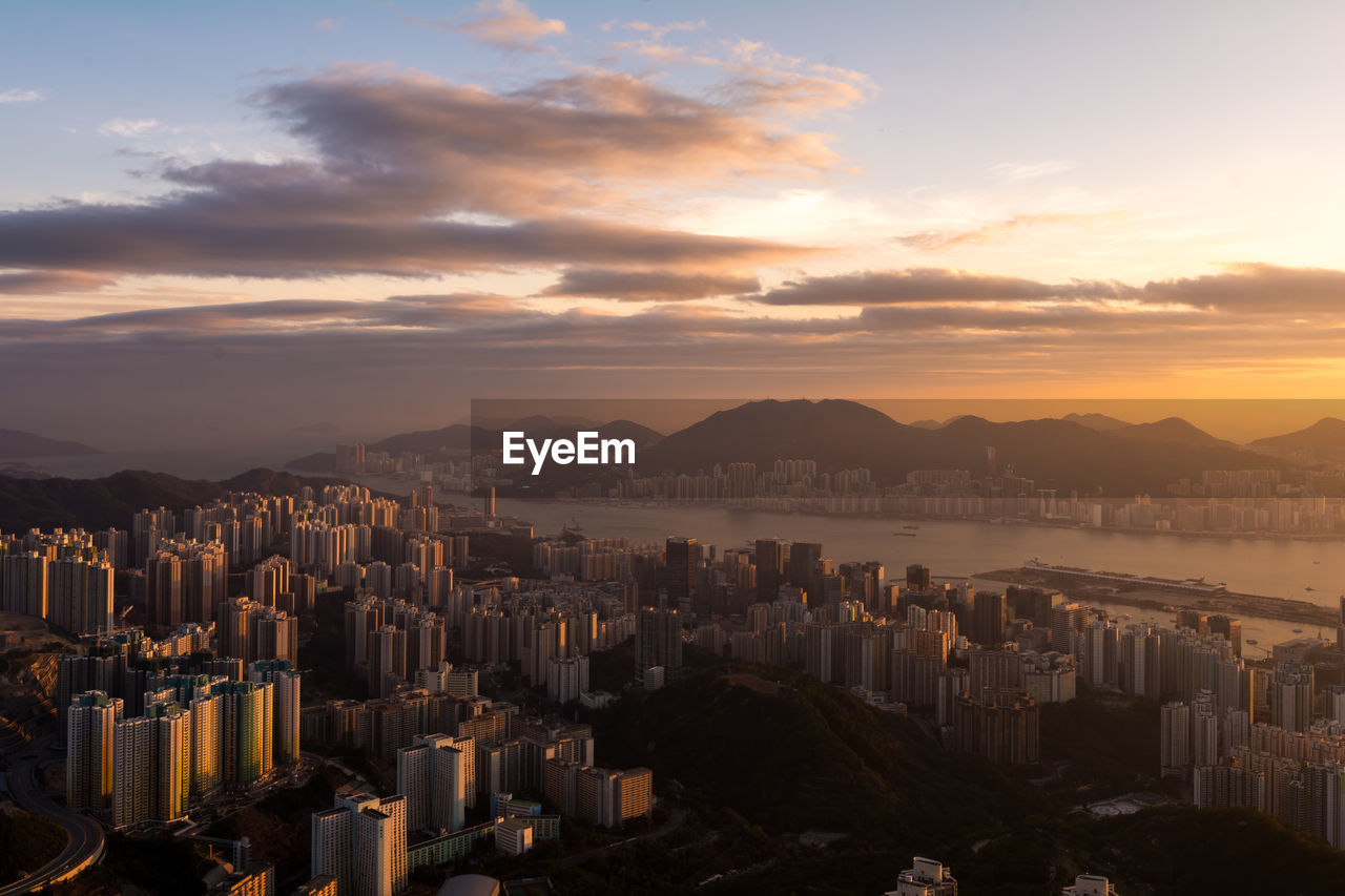 Cityscape by sea against sky during sunset