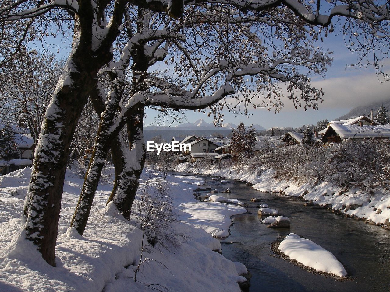 Scenic view of river flowing in village against cloudy sky