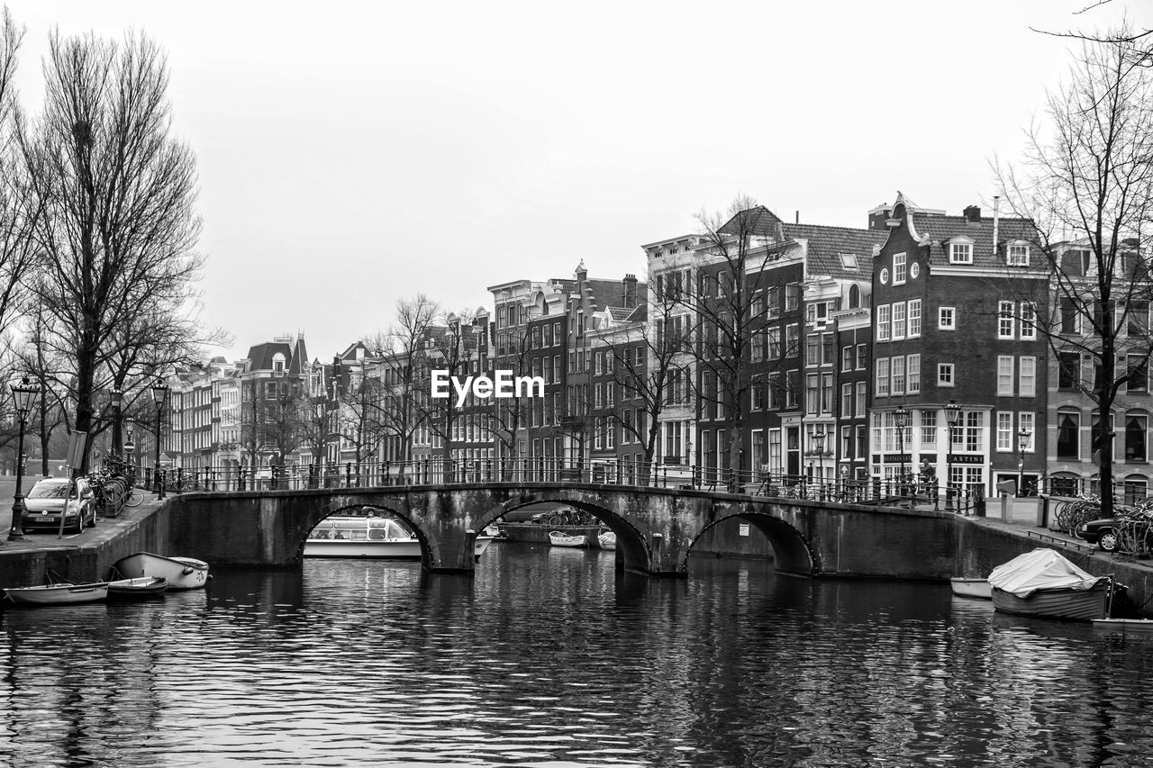 BRIDGE OVER RIVER BY BUILDINGS AGAINST SKY