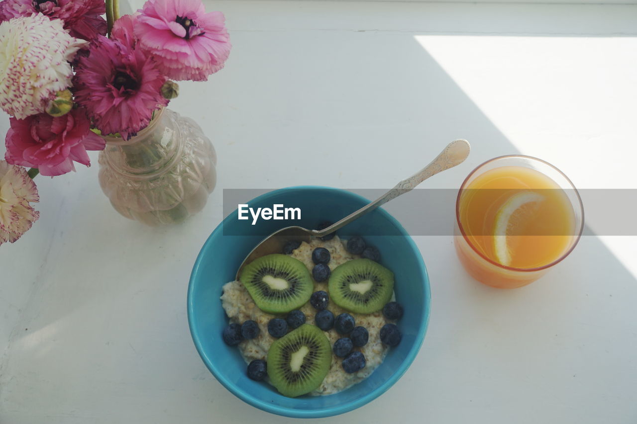 High angle view of oatmeal with juice by flower vase on table