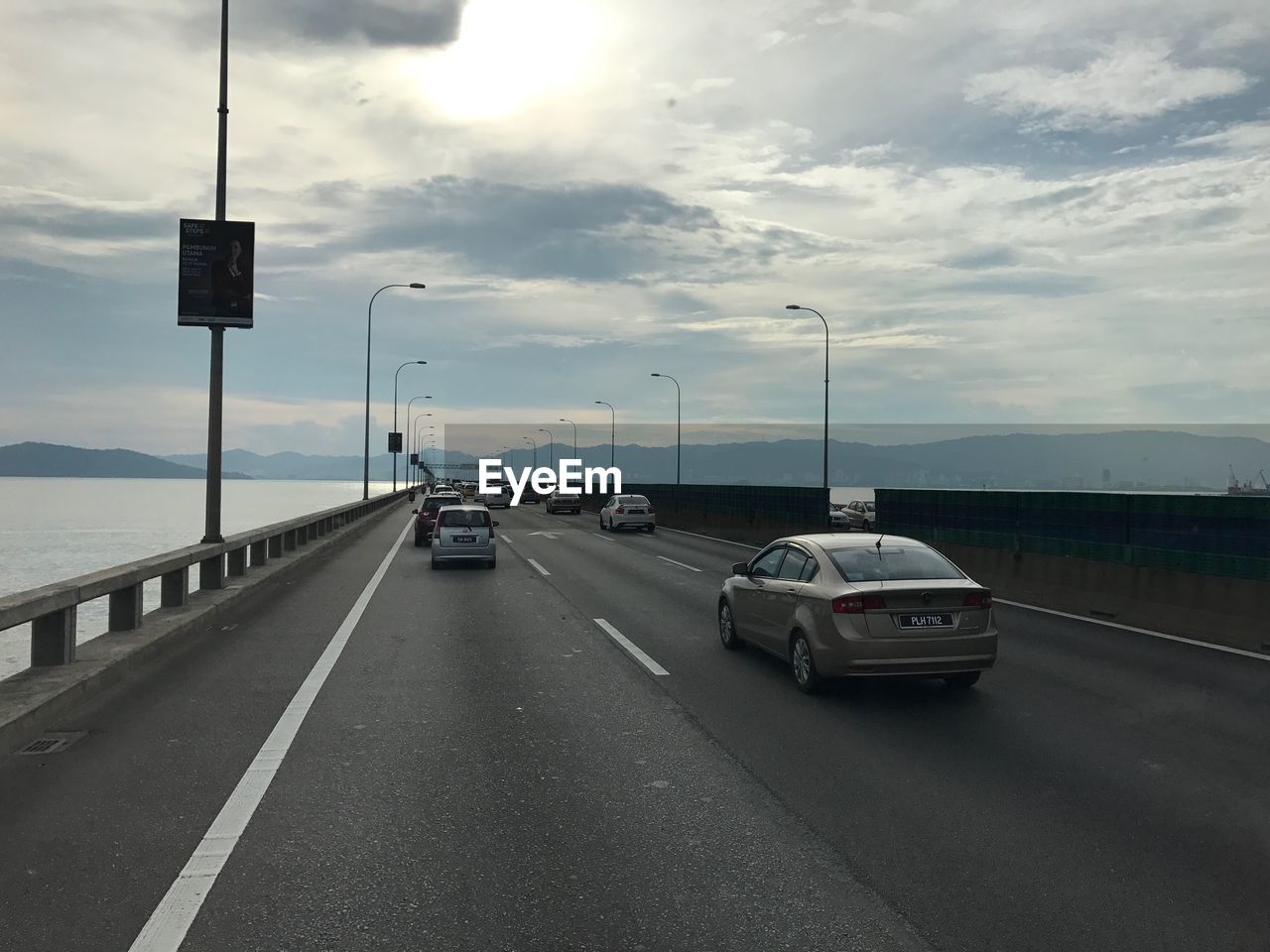 CARS ON ROAD BY SEA IN CITY AGAINST SKY