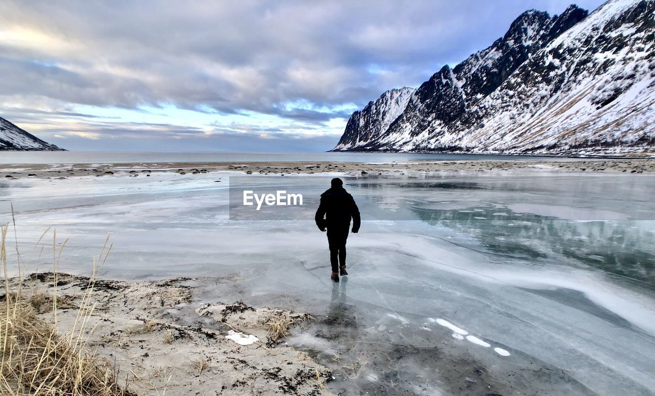 Rear view of man walking on frozen lake against snowcapped mountain