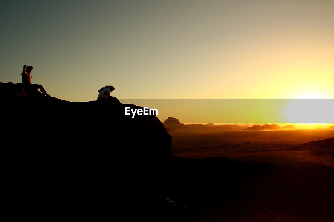 SILHOUETTE PEOPLE ON ROCK DURING SUNSET