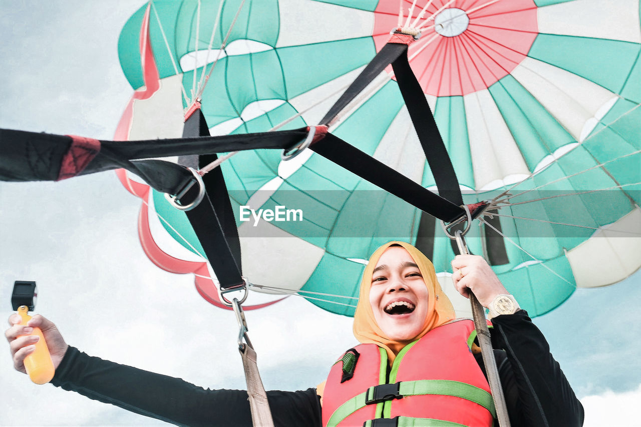 Low angle view of happy young woman paragliding against sky