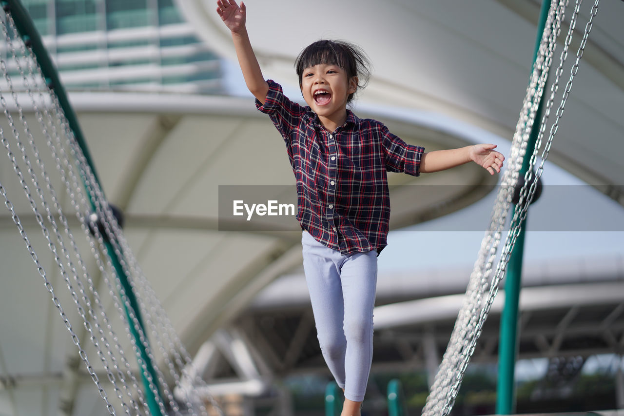 Cheerful girl screaming on play equipment against buildings