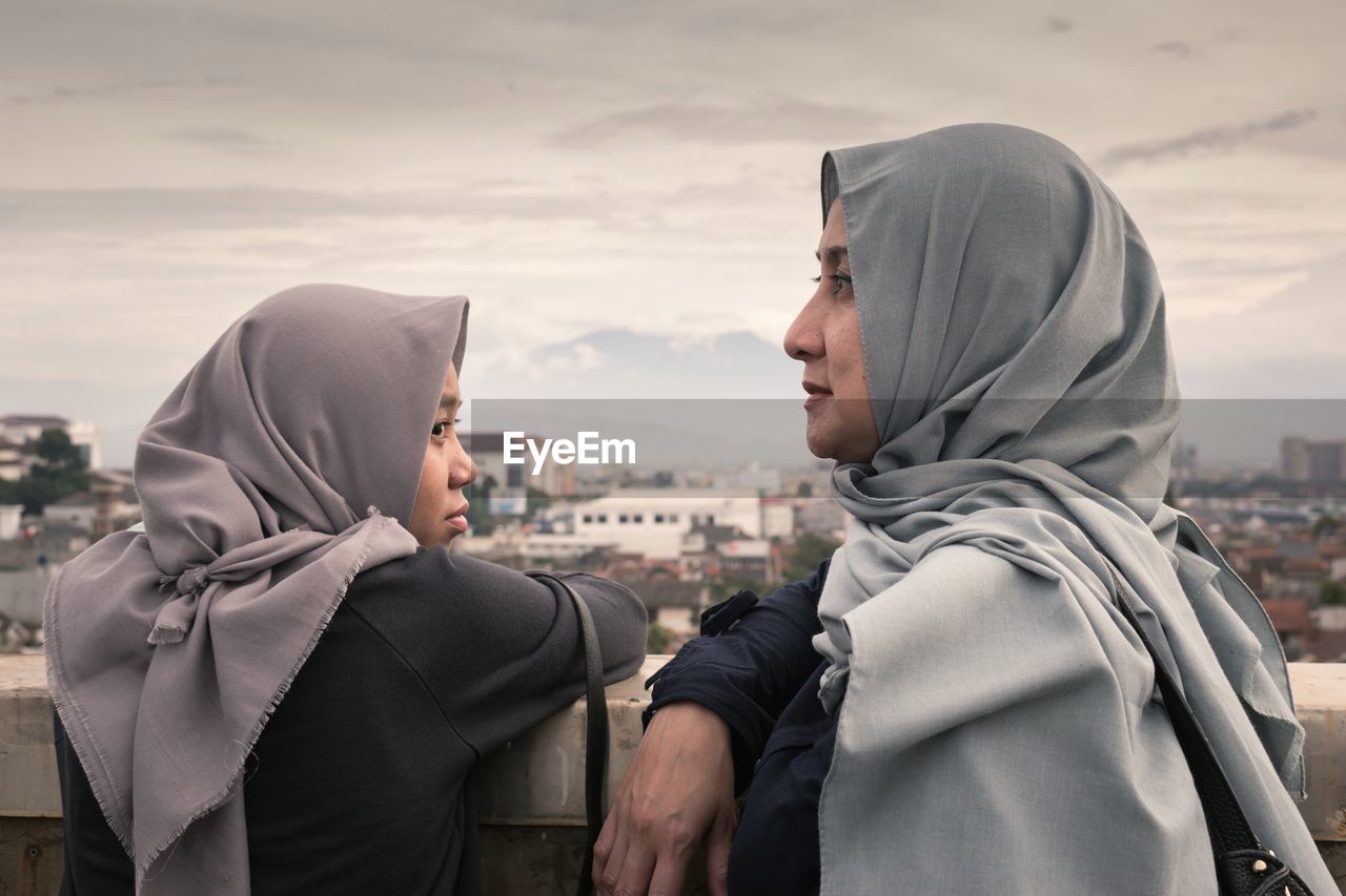 Close-up of mother and daughter standing in city against sky