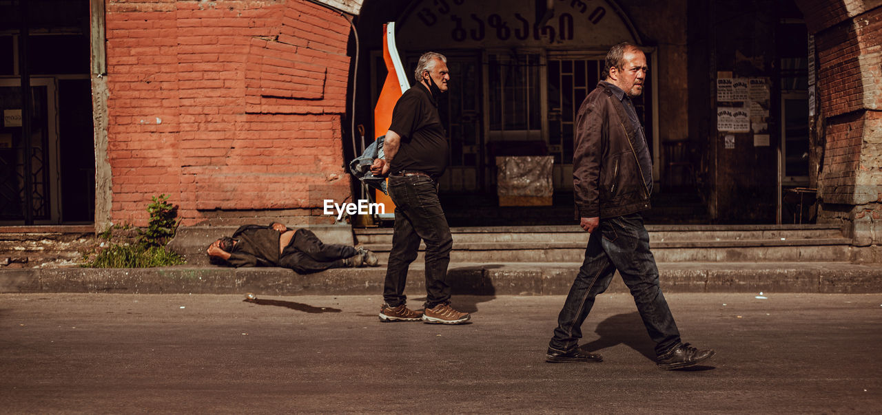 MAN STANDING ON STREET AGAINST BUILDING