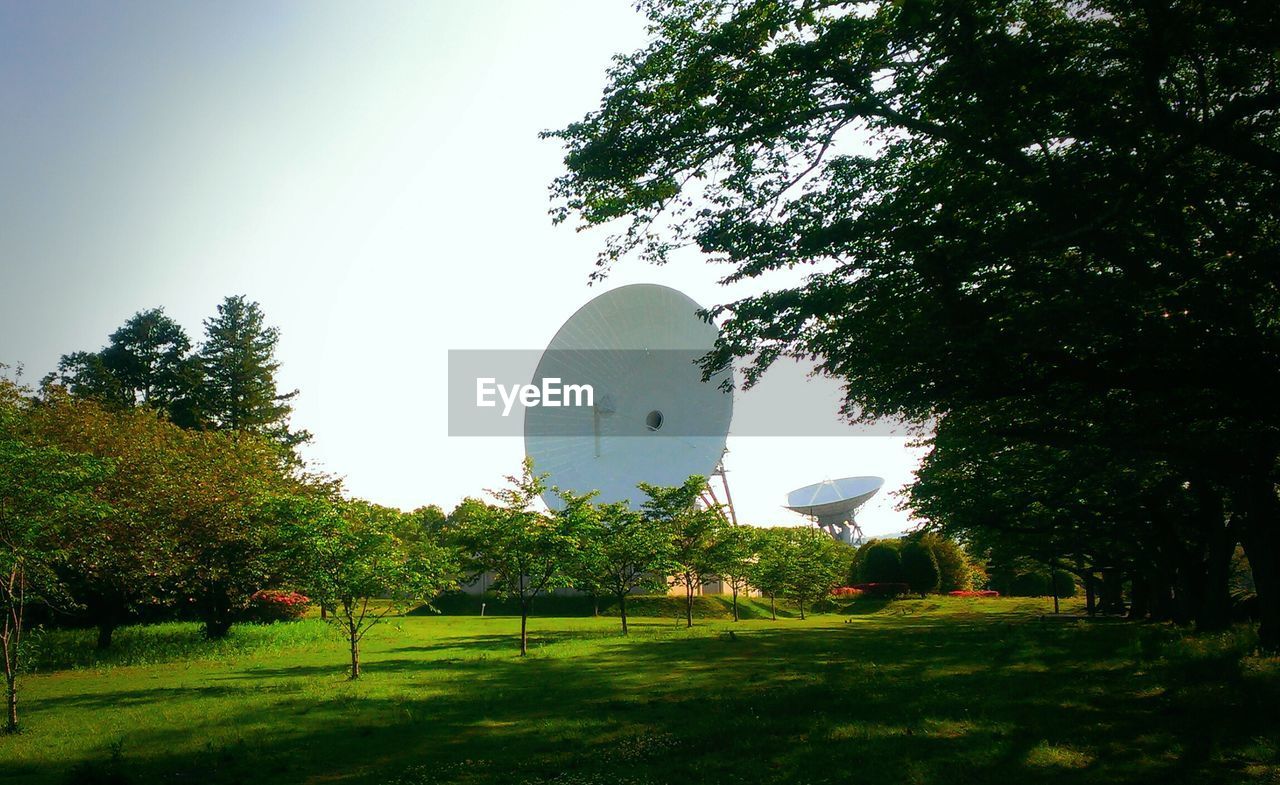 Trees on landscape with satellite dishes against clear sky