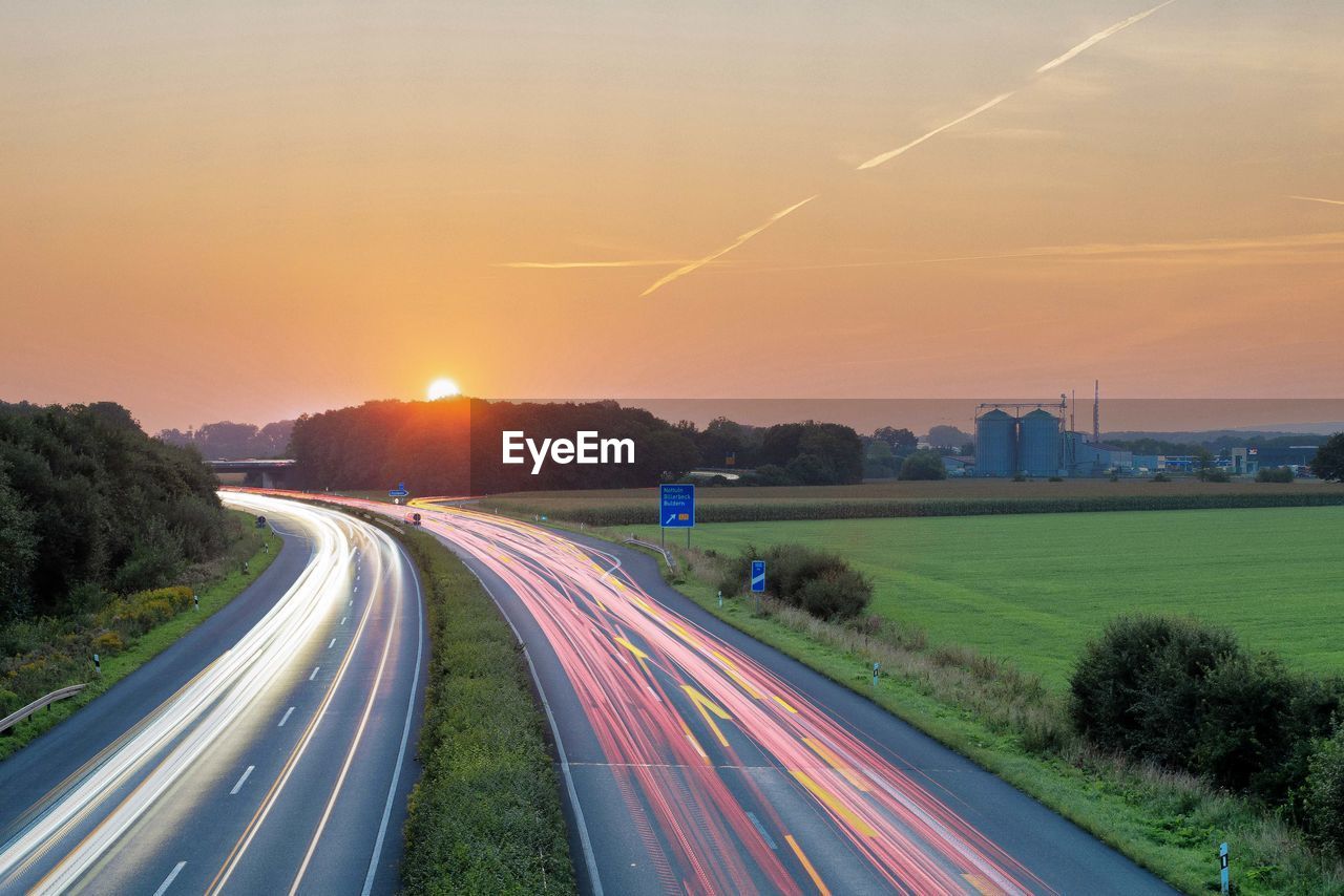 LIGHT TRAILS ON HIGHWAY DURING SUNSET