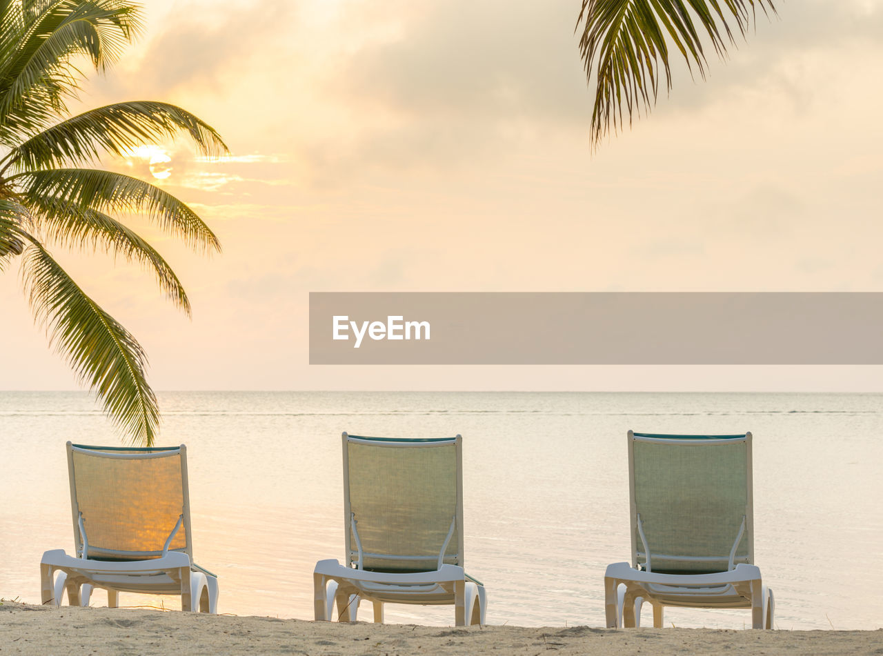 CHAIRS AND TABLES ON BEACH AGAINST SKY