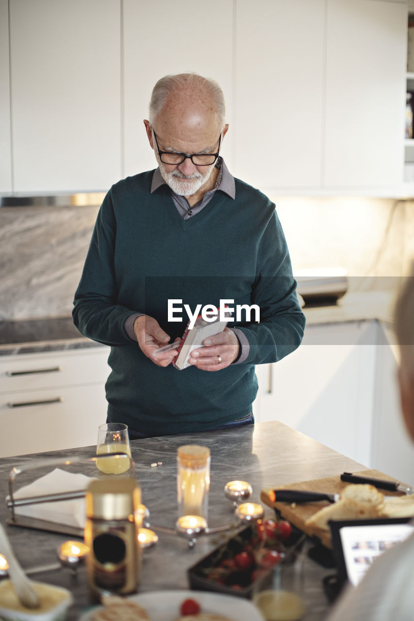 Senior man taking pills while standing by kitchen island at home