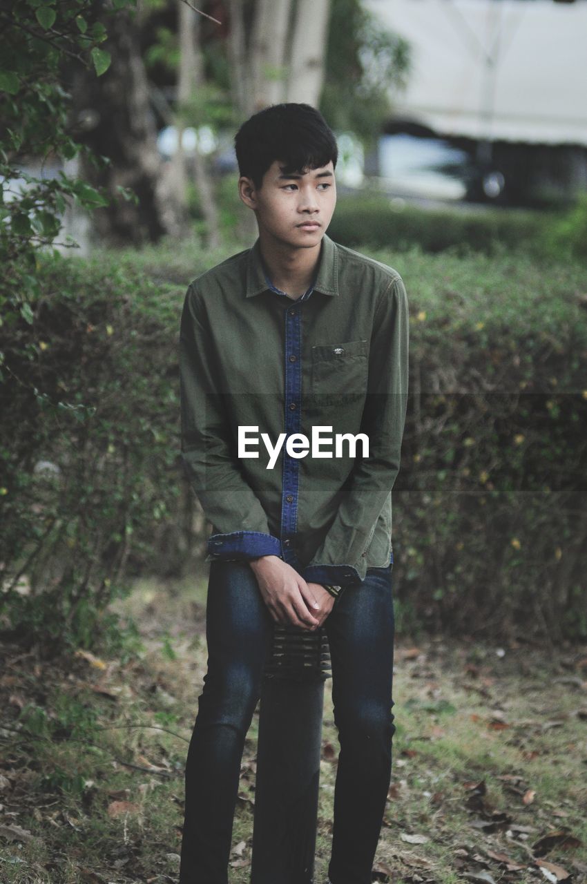 Young man looking away while standing on land