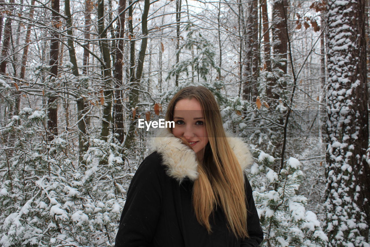 Portrait of beautiful young woman in warm clothing standing at forest during winter