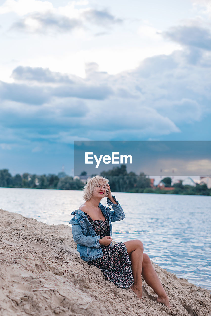 Rear view of woman sitting on beach against sky