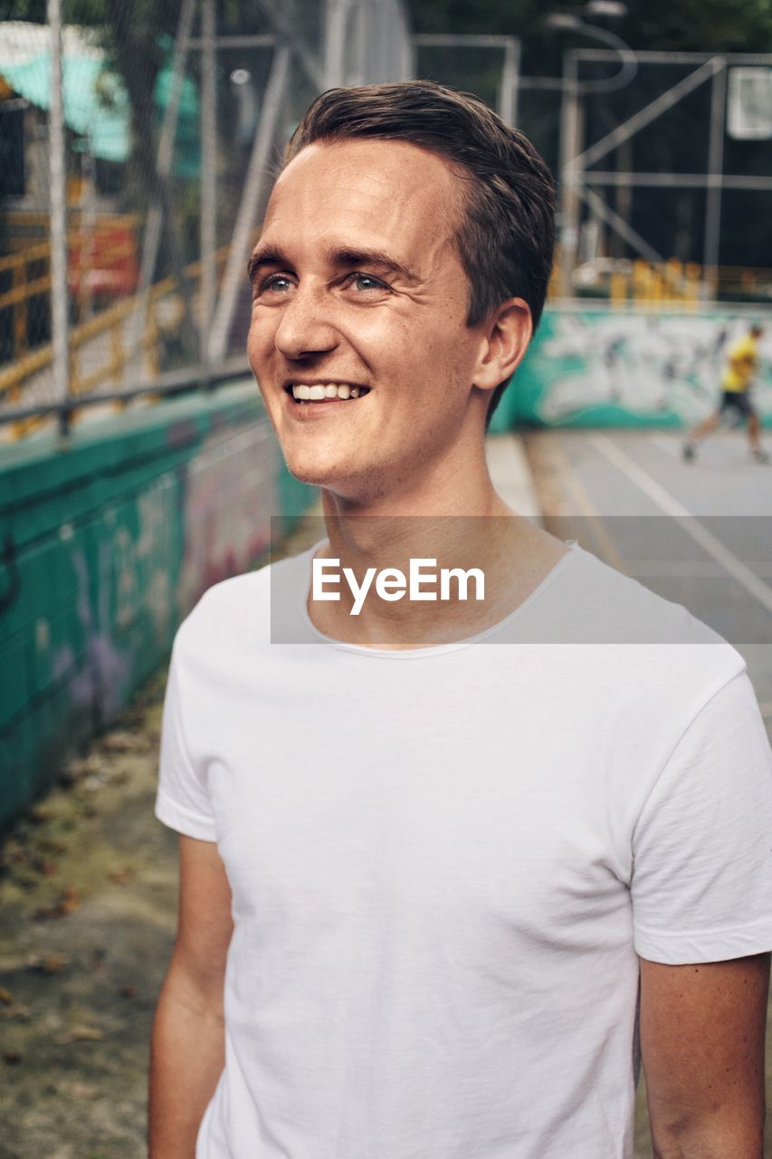 Smiling young man standing by basketball court 