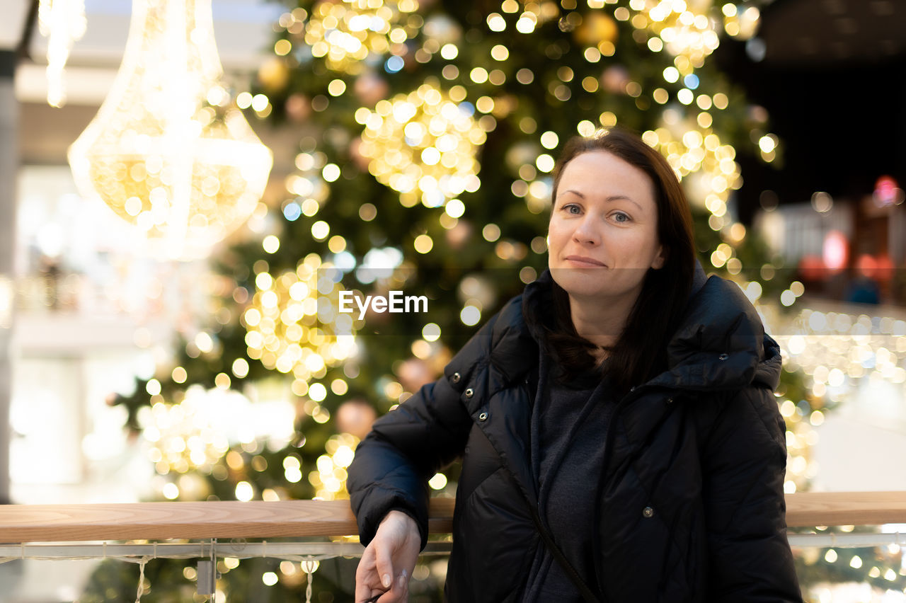 Portrait of a beautiful woman on  background of a christmas tree with bright lights gerlant.  