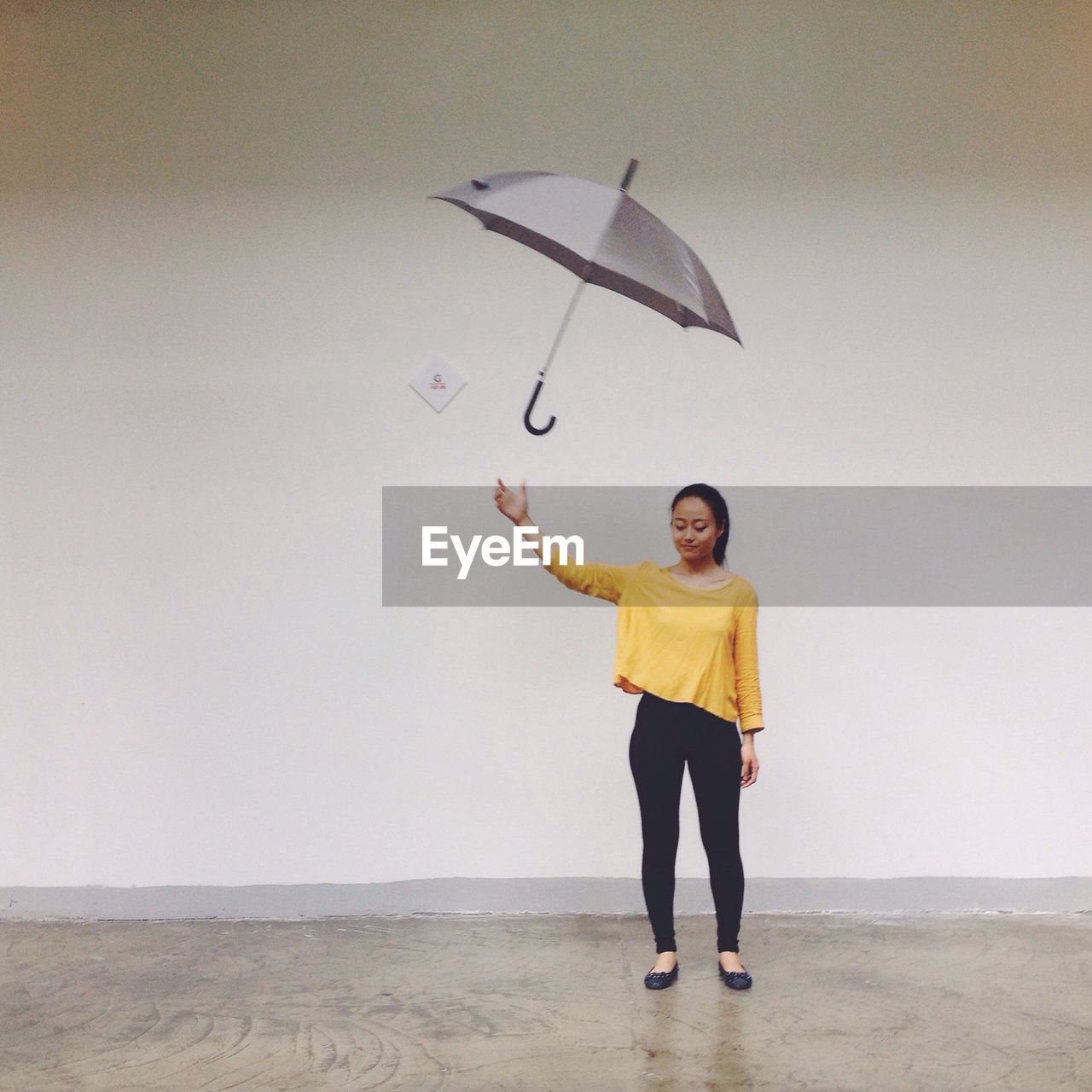 Full length of mid adult woman throwing umbrella while standing against wall