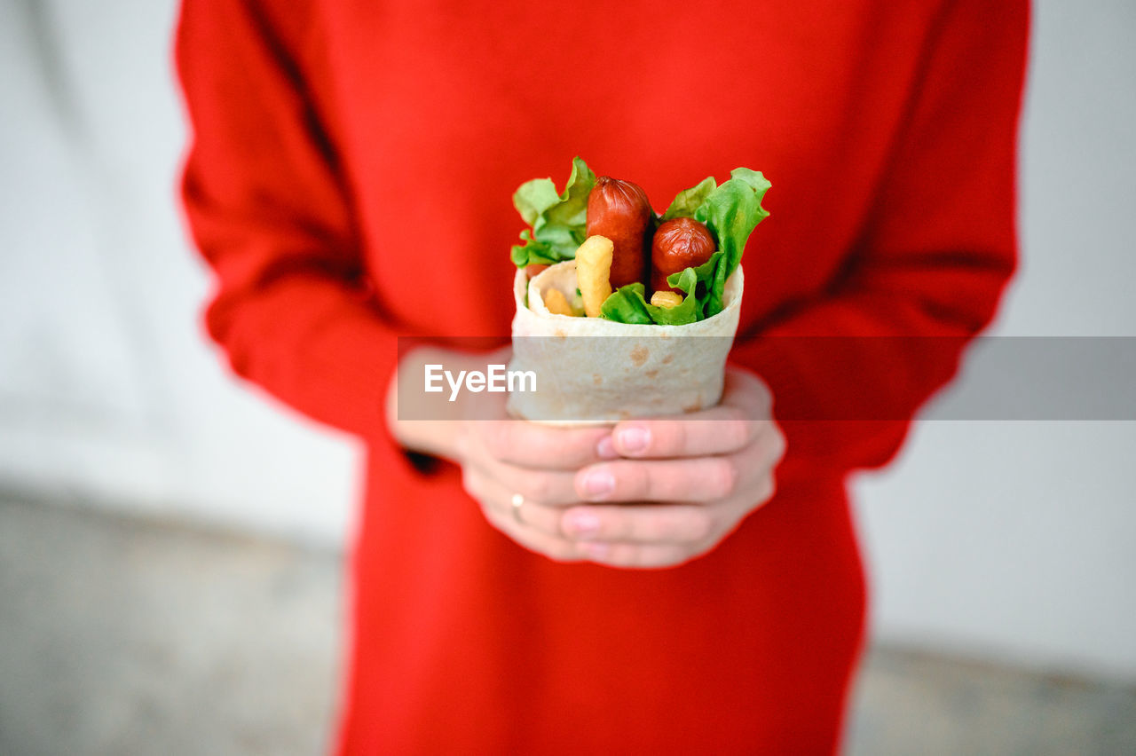 The hands of a girl in red clothes are holding fast street food. shawarma is food in pita