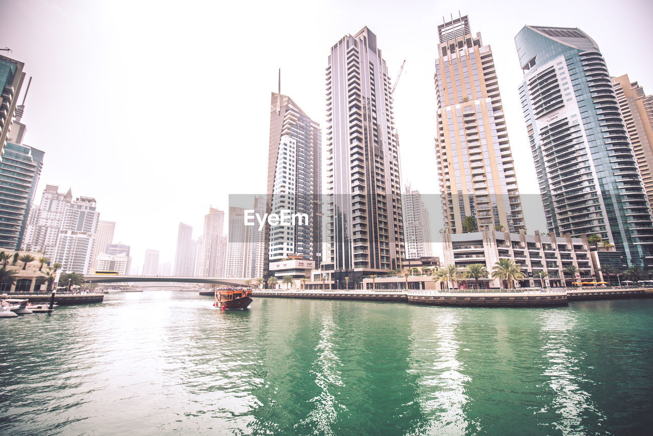 View of modern buildings by river against sky